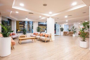 En rummelig lobby med et moderne design, med et siddeområde med sofaer og stole, et træbord og potteplanter.