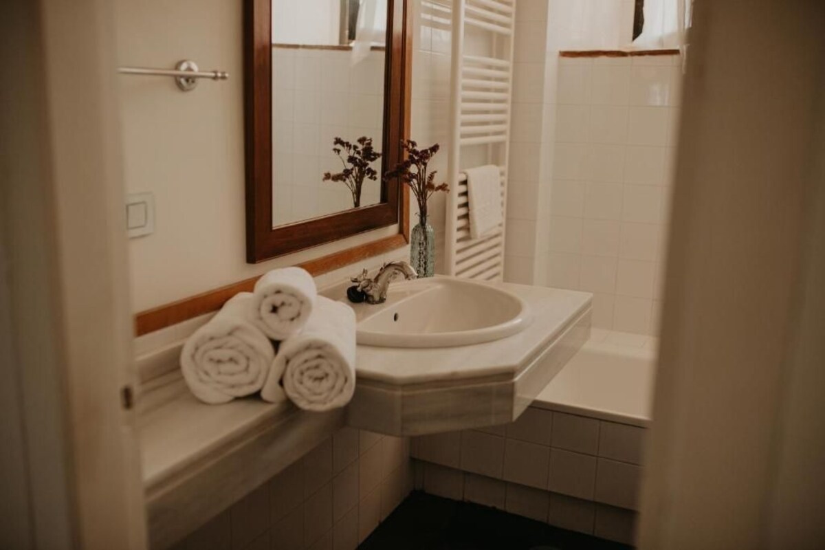 Un baño con lavamanos, espejo, toallero y dispensador de toallas.