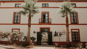 A building with a red and white facade, multiple windows, and a central entrance with a black door. - Hotel Posada de Valdezufre (Aracena)