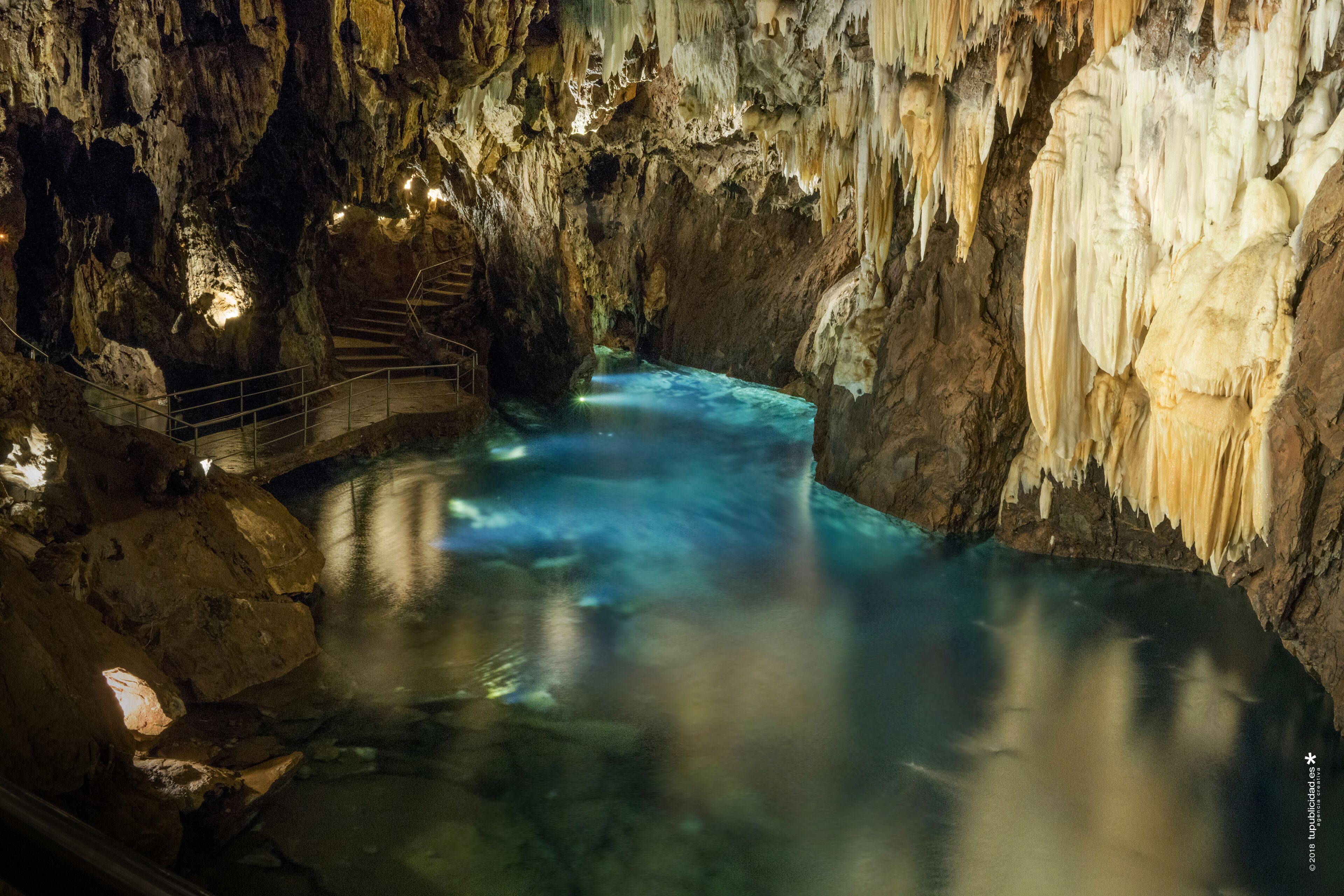 Una cueva con un arroyo, escaleras y una barandilla.