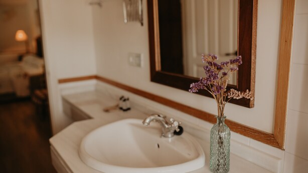 Un baño con un lavamanos blanco, un espejo y un florero con flores secas.