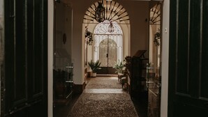 A hallway with a patterned floor, a large arched window, and potted plants. - Hotel Posada de Valdezufre (Aracena)