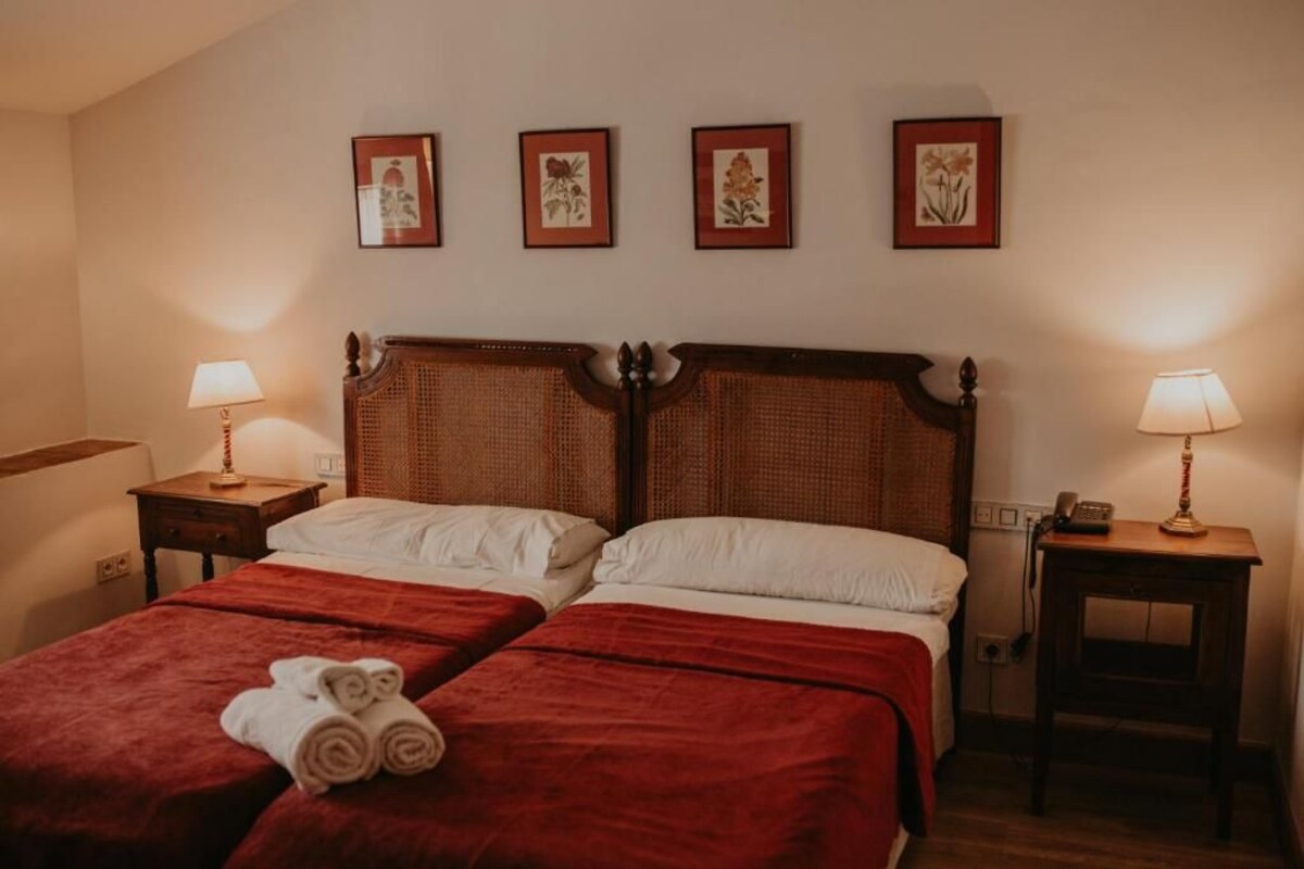 Una cama doble con ropa de cama roja, dos mesitas de noche con lámparas y cuatro cuadros enmarcados en la pared.