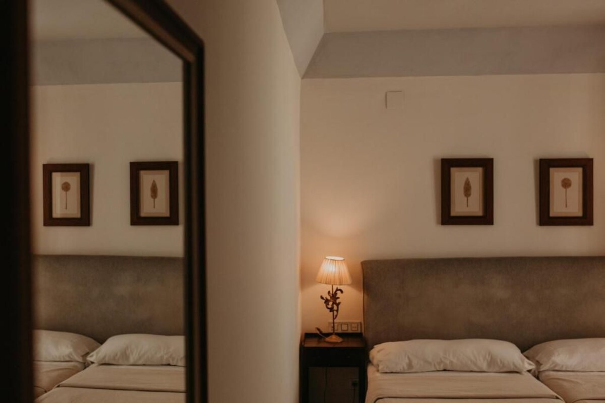 Una habitación de hotel con dos camas, una mesita de noche con lámpara y cuadros en la pared.