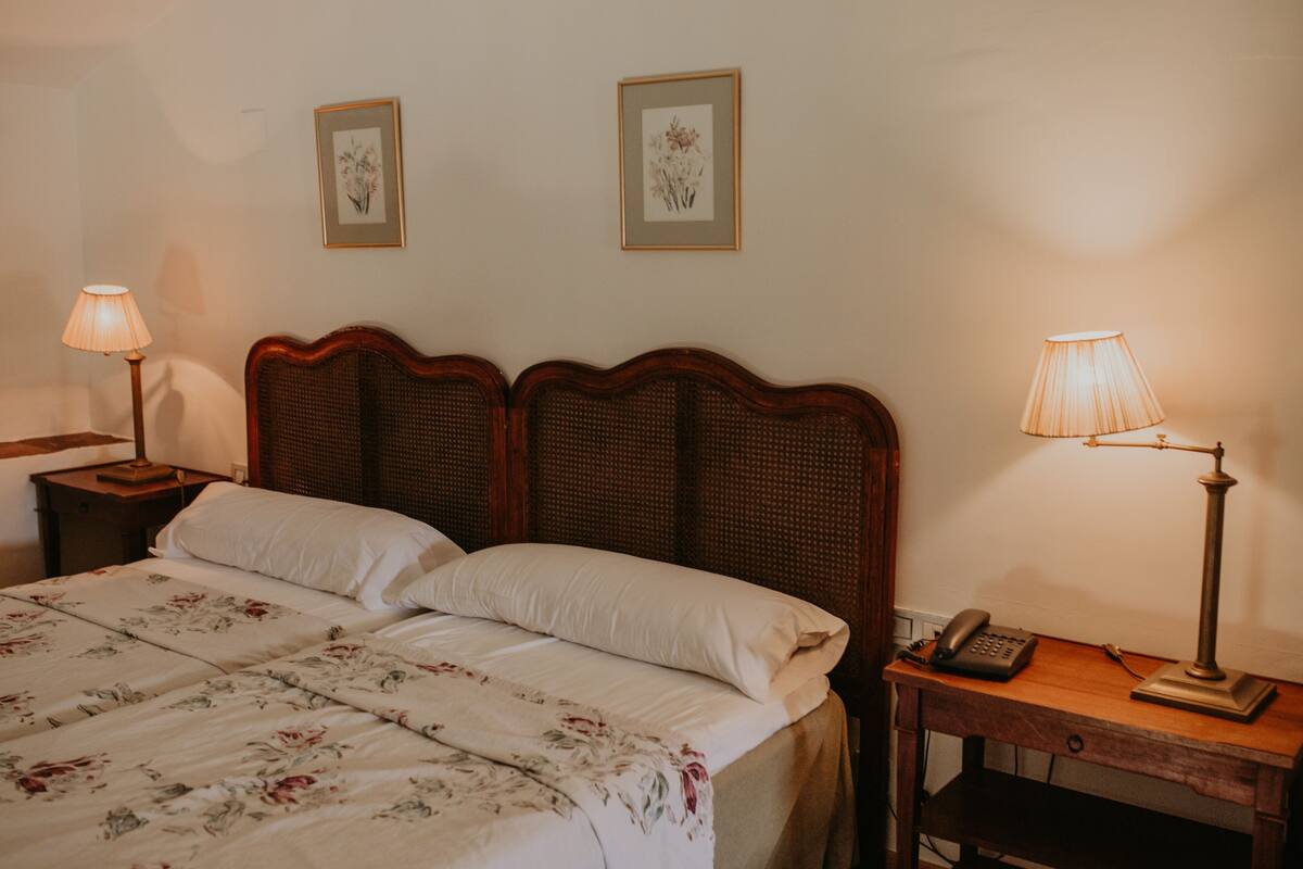 A neatly made bed with floral bedding, two bedside lamps, and a small wooden nightstand with a telephone.