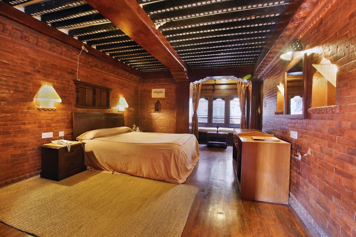 A cozy room with a wooden ceiling, brick walls, a bed, bedside tables, and a desk.