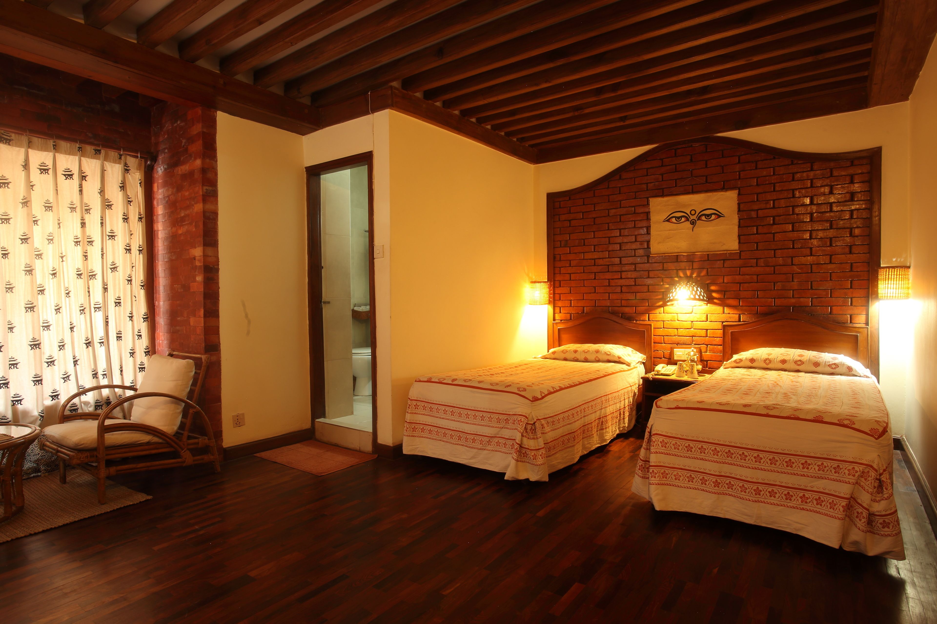 A room with two beds, wooden flooring, a brick accent wall, and a wooden ceiling.