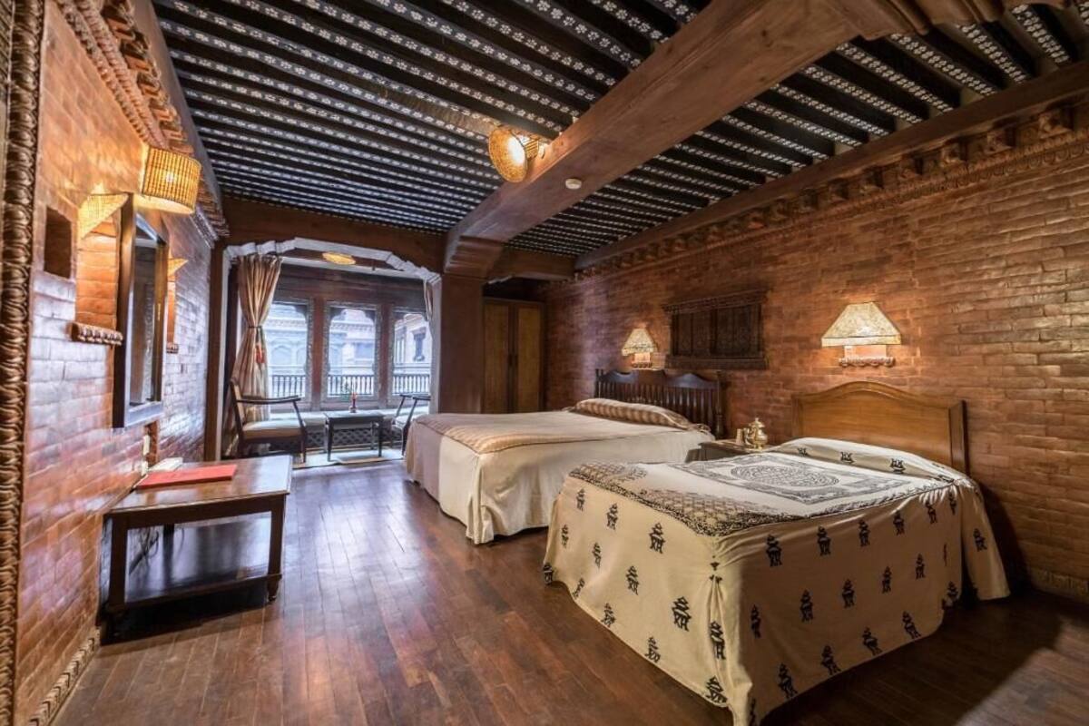 Una habitación tradicional con dos camas, vigas de madera, paredes de ladrillo y techo inclinado.