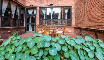 Edificio de ladrillo con patio central que incluye una mesa y sillas, rodeado de plantas verdes grandes.
