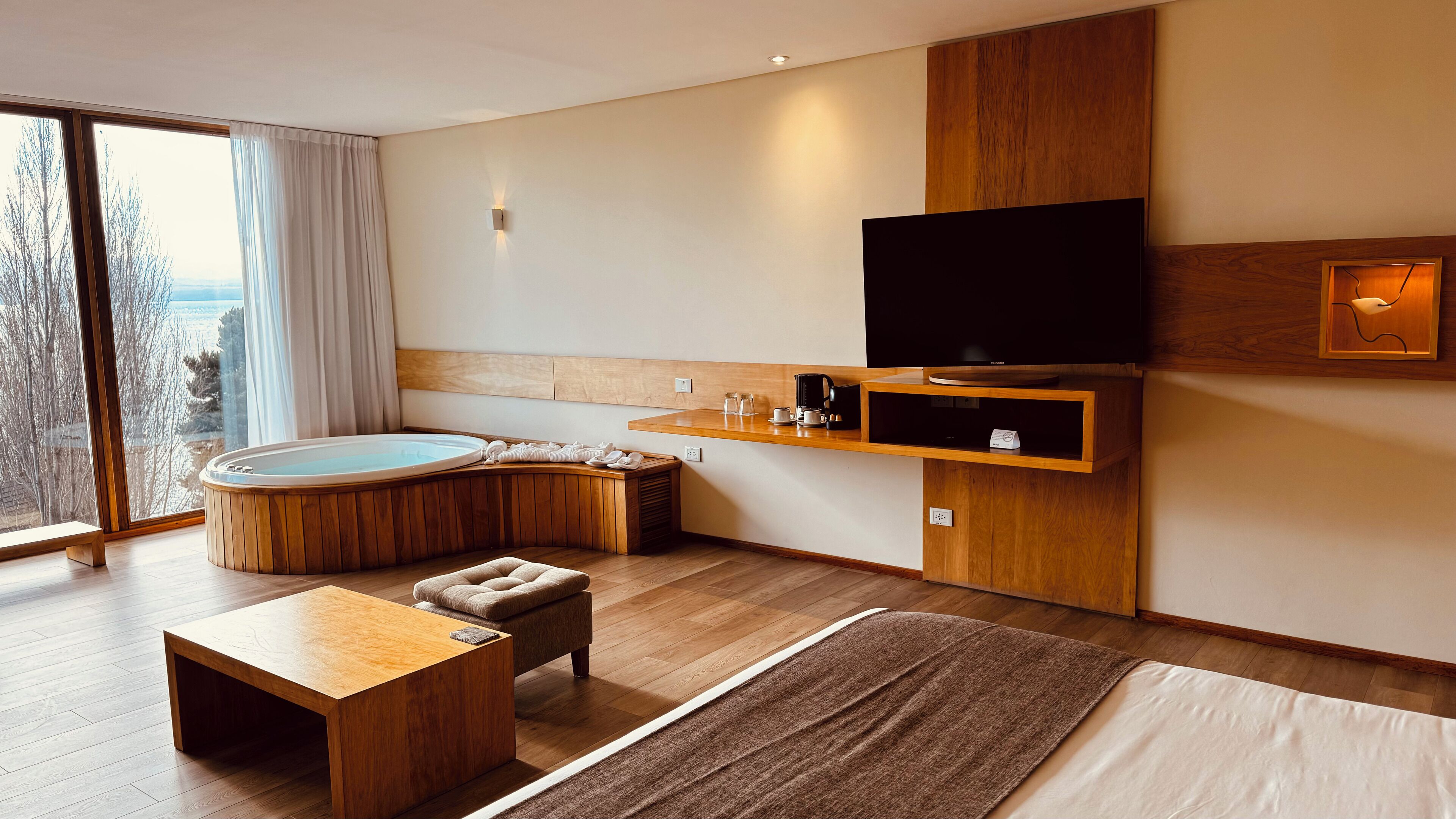 Ein modernes Wohnzimmer mit Holzboden, großem Fenster und Ausblick, integriertem Fernseher, Kaffeemaschine und einer gemütlichen Sitzecke.