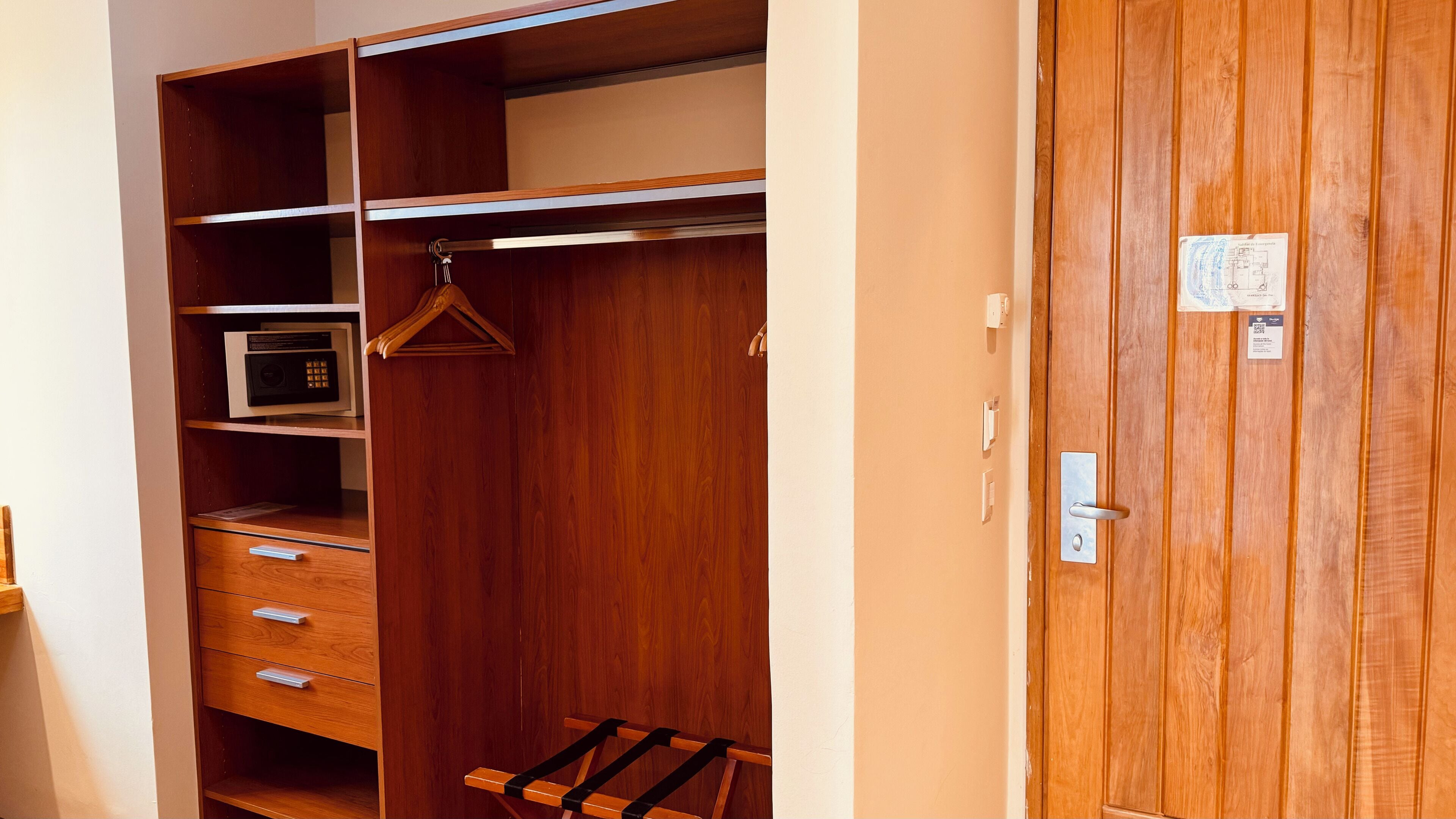 Une armoire en bois avec plusieurs étagères, une tringle pour suspendre les vêtements et un petit meuble à tiroirs.