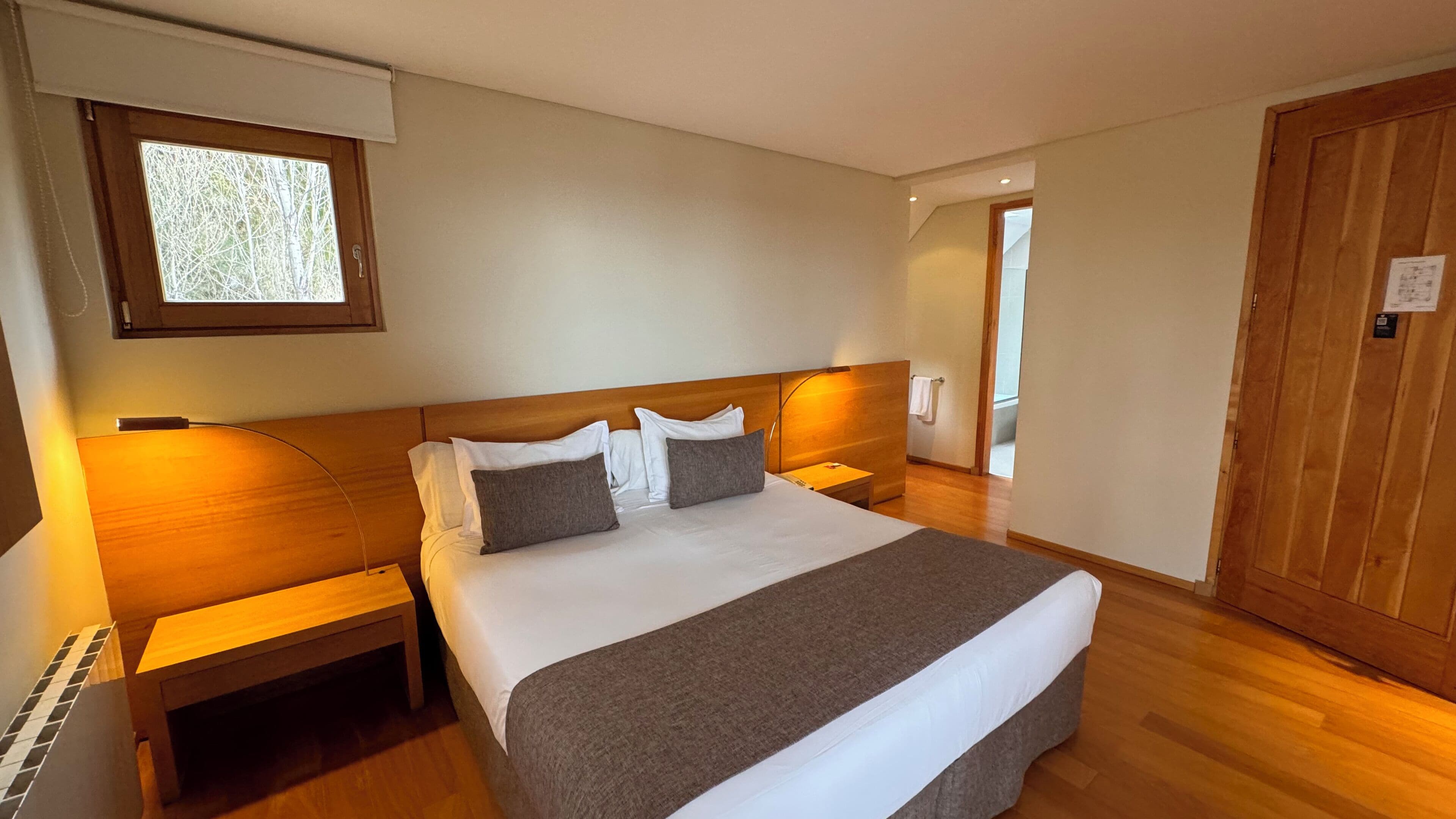 Un dormitorio con una cama grande, cabecera de madera, mesitas de noche, una ventana y una puerta.