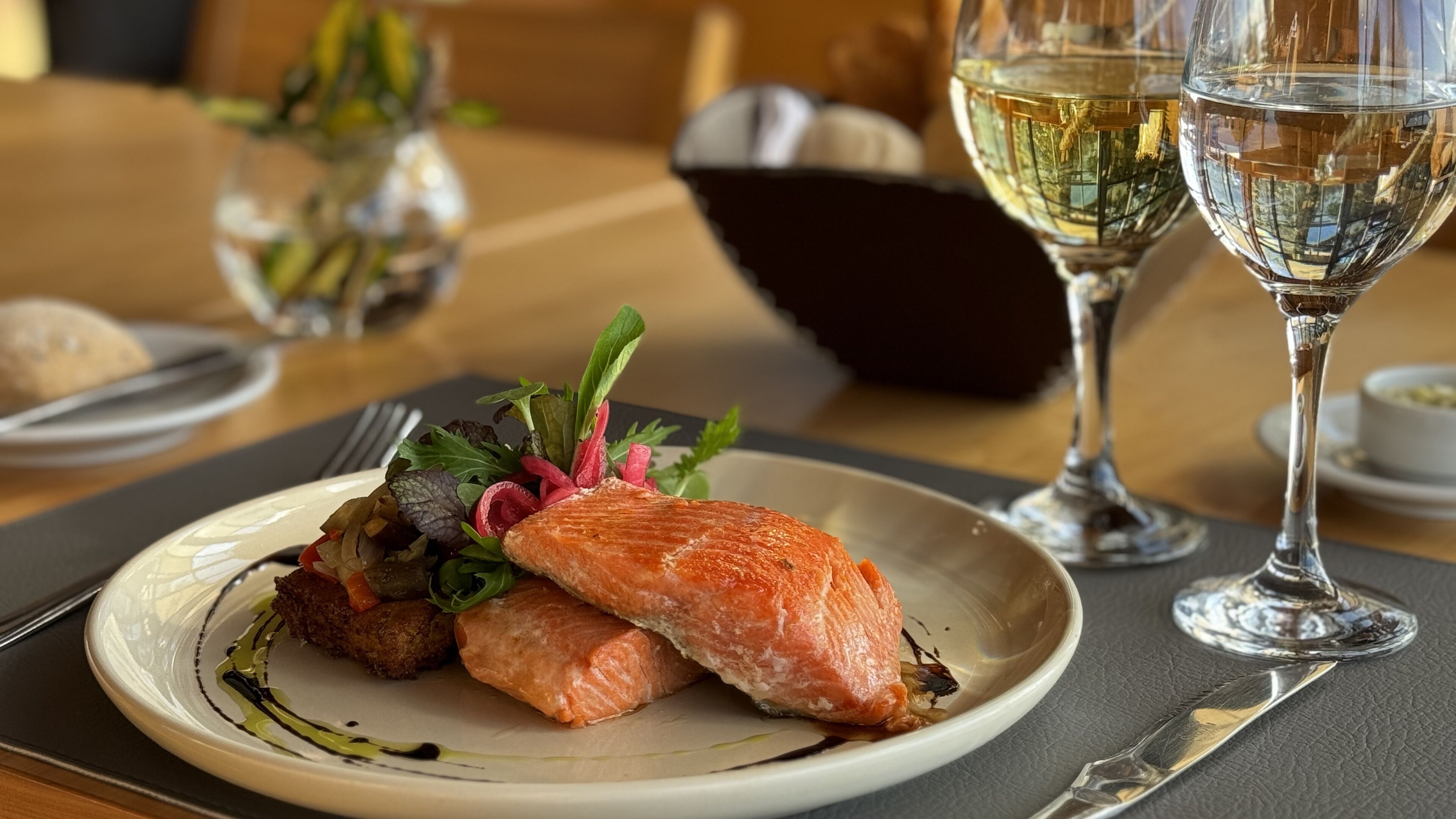 Ein Teller mit Lachs und Grünzeug, ein Glas Weißwein und eine dunkle Flasche im Hintergrund.