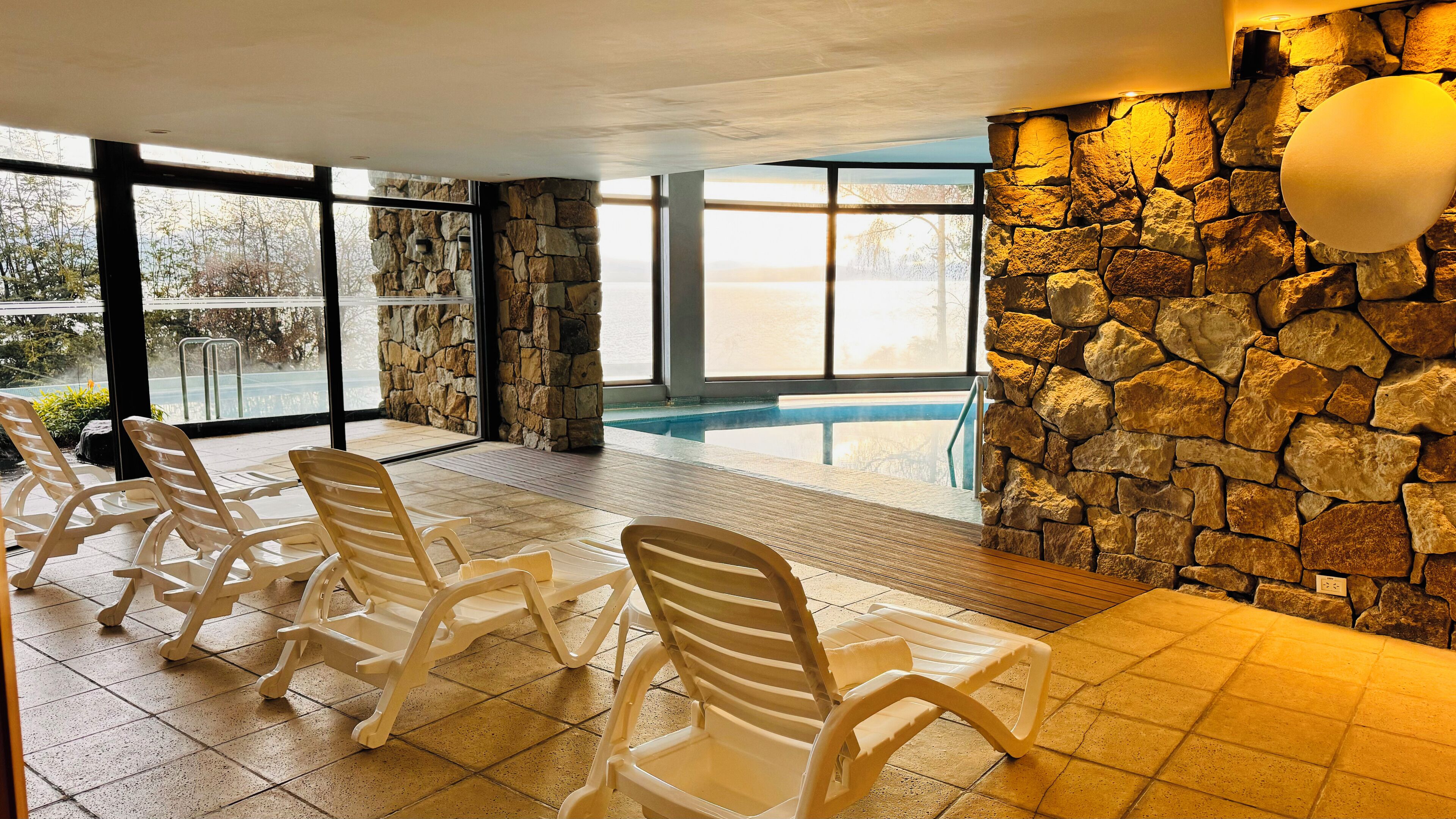 A poolside area with stone walls, large windows, and plastic lounge chairs.