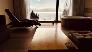 Un soggiorno moderno con un tavolino in legno, una poltrona in pelle e vista su un lago e montagne attraverso ampie finestre.