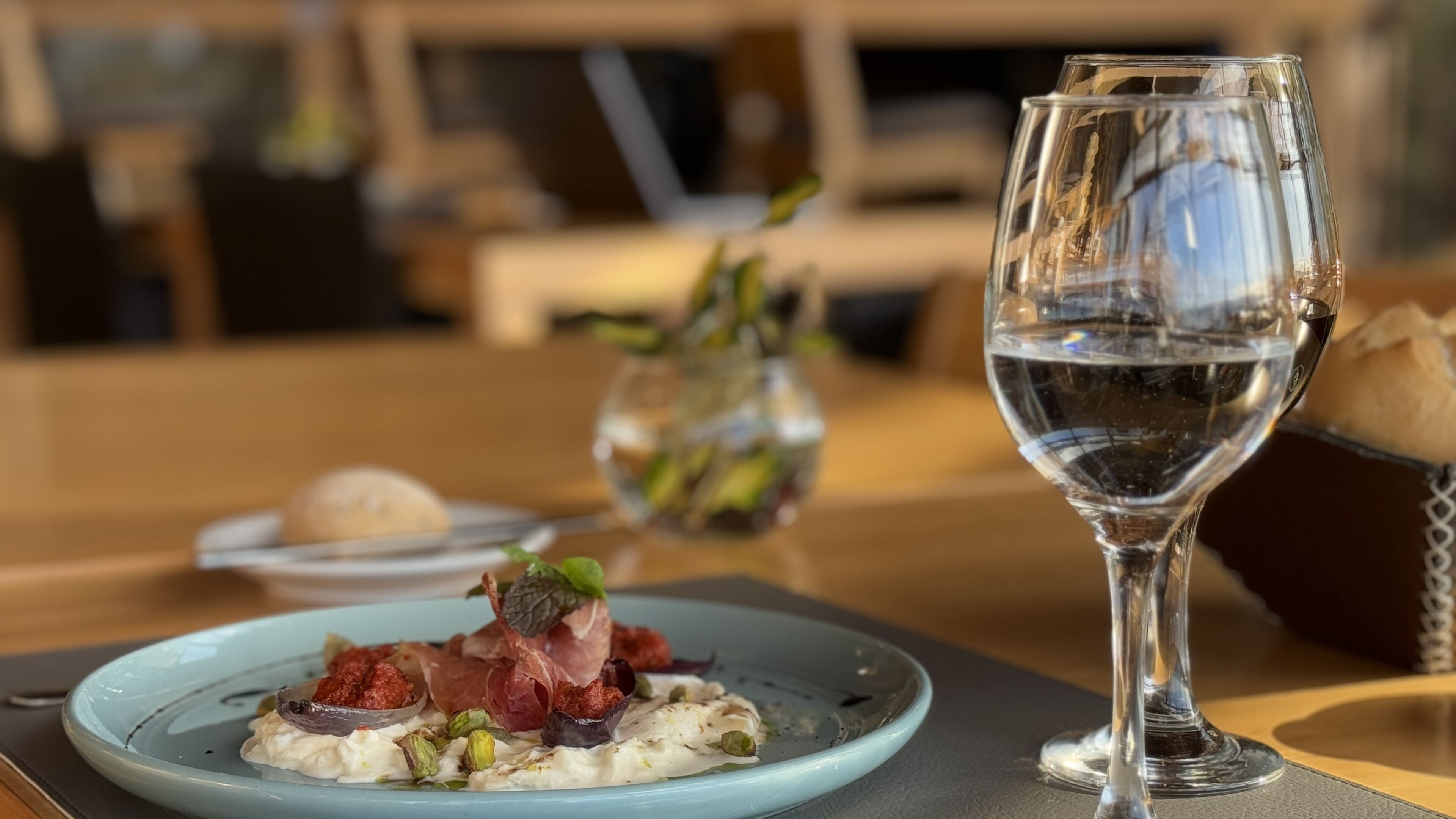 Une table à manger avec une assiette de nourriture, un verre d’eau et un vase rempli de fleurs.