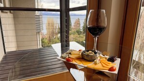 Un balcone con un tavolo apparecchiato per un pasto, un bicchiere di vino rosso e una vista panoramica su alberi e montagne.