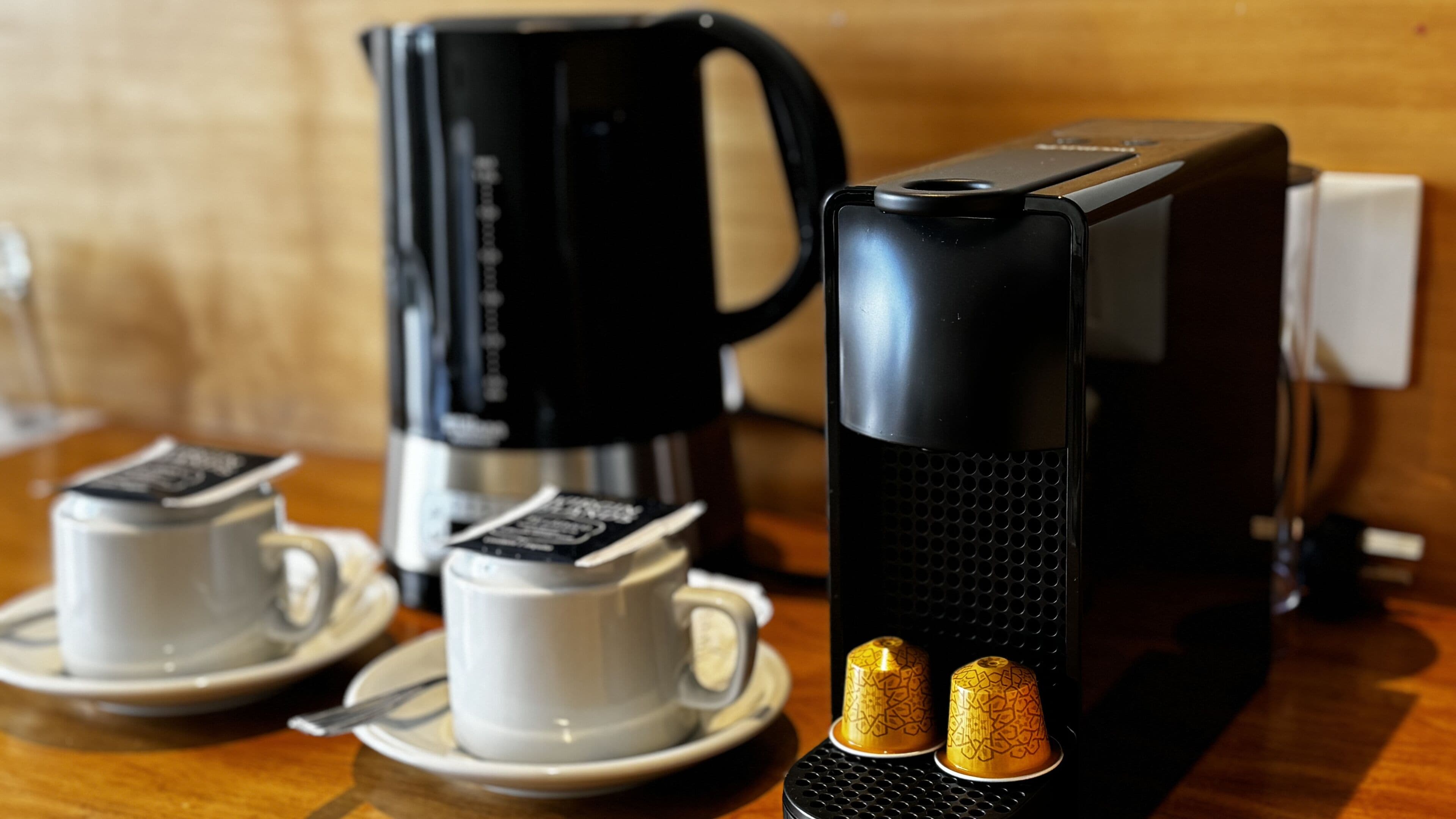 A coffee maker, two cups, and a kettle on a wooden table.