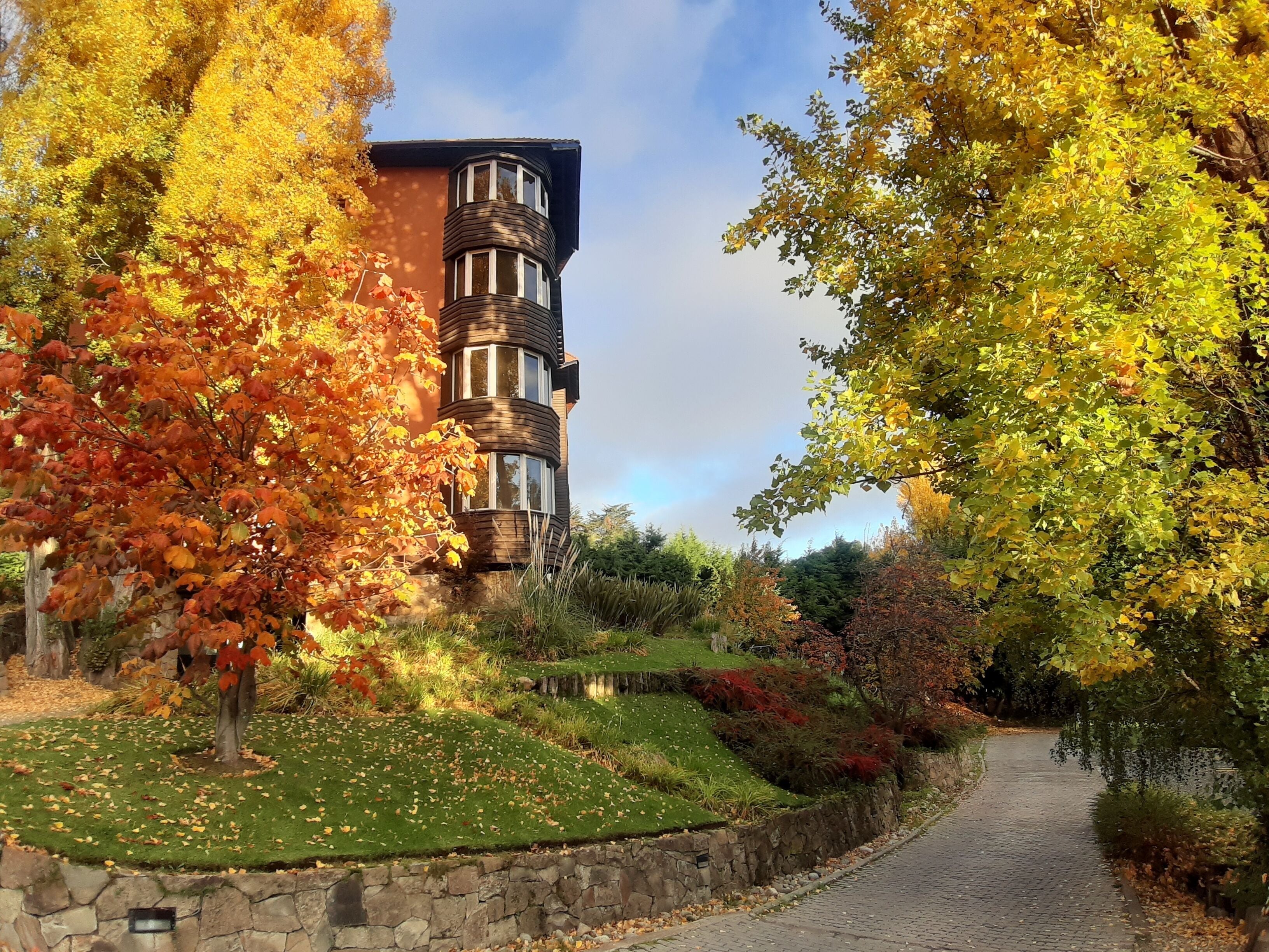 A building with a curved facade and multiple windows, surrounded by trees with autumn foliage.