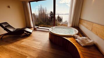 Relax in a serene spa room with a spacious hot tub, lounge chair, and scenic lake views.