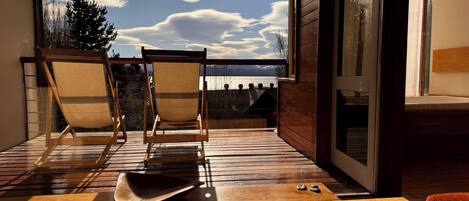 Un balcon doté d’un plancher en bois, de deux chaises et d’une table sur laquelle se trouvent un chapeau et des pierres.