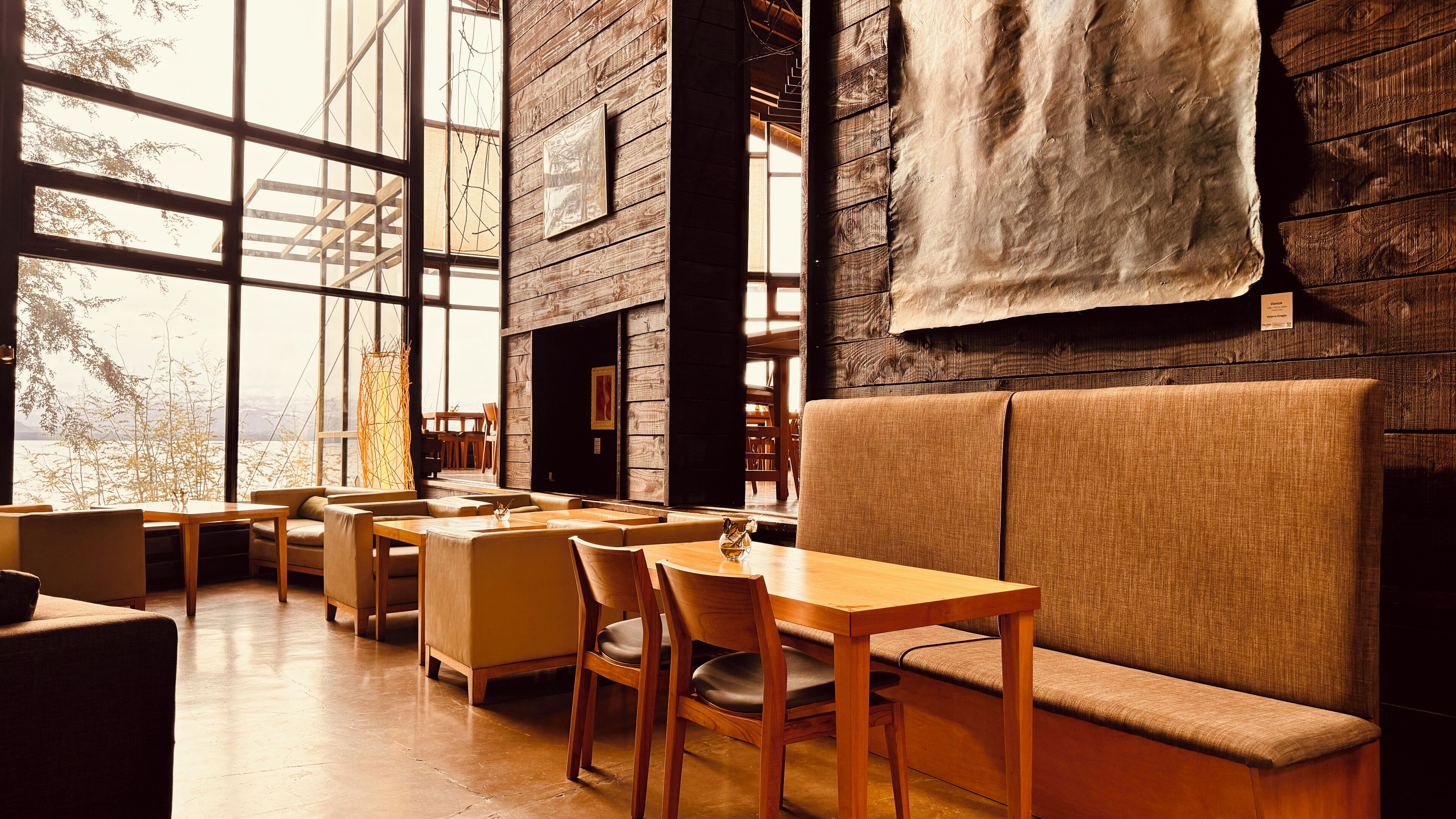 A cozy, well-lit cafe with wooden furniture and large windows offering a view of the outdoors.