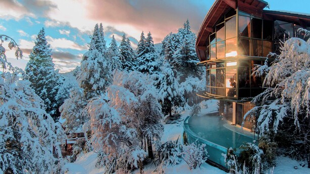 Una moderna baita con piscina vetrata circondata da alberi innevati.
