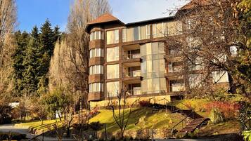 A multi-story building with balconies, surrounded by trees and a grassy area.
