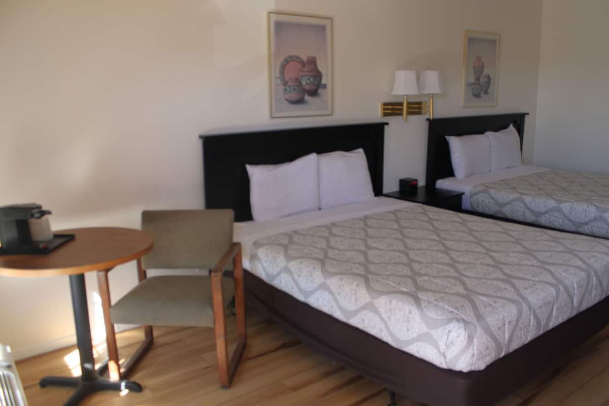 A hotel room with two beds, a small table, a chair, and a nightstand with lamps.