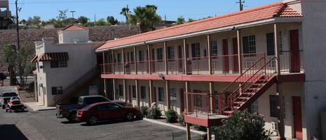 A two-story motel with a red-tiled roof, multiple balconies, and a parking area with several cars.