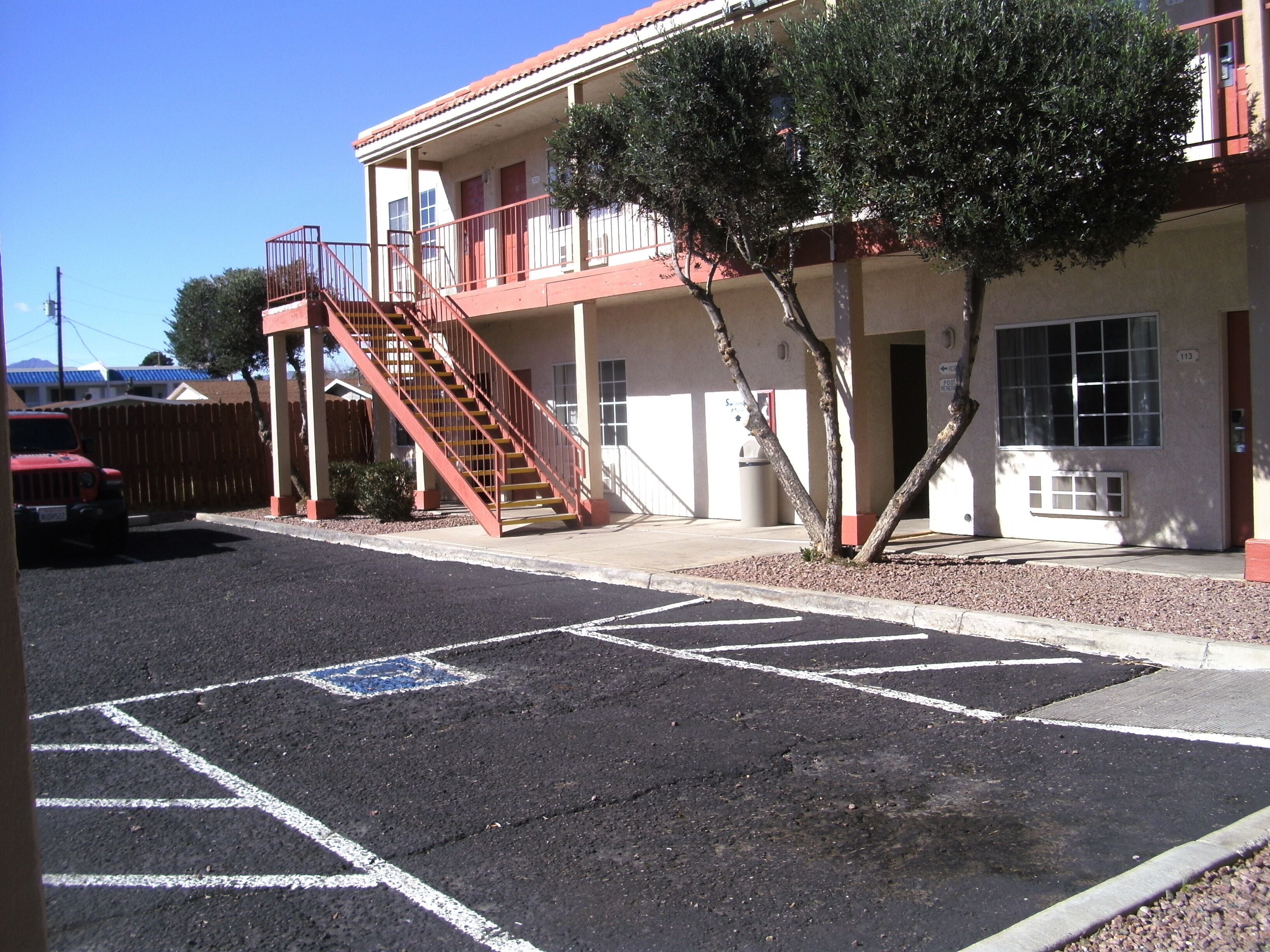 A building with a red staircase, a parking lot with marked spaces, and a tree in front.