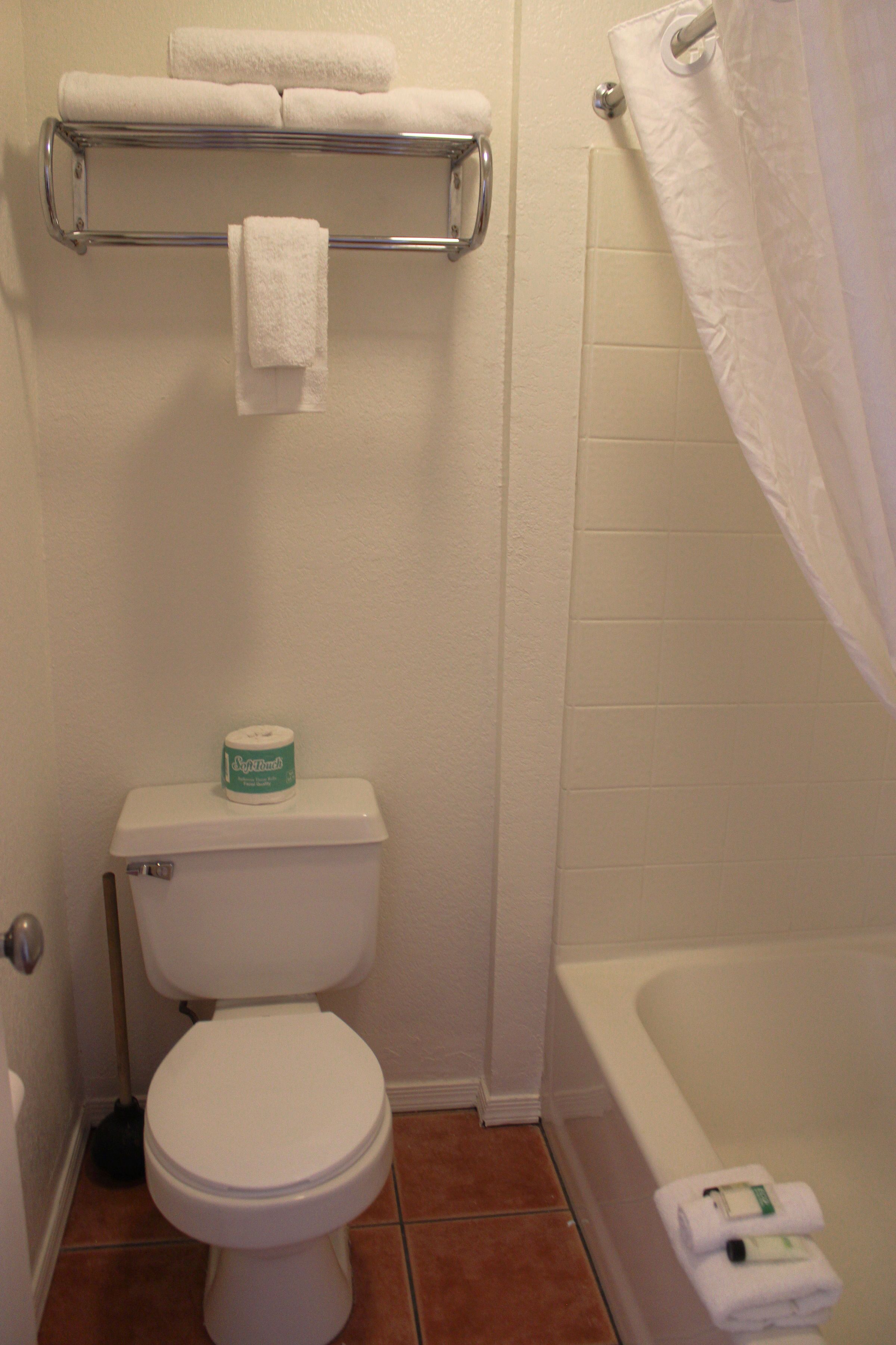A bathroom with a toilet, a towel rack with towels, a roll of toilet paper, and a bathtub.