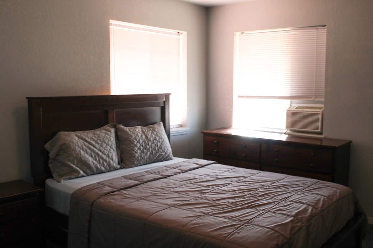 A bedroom with a bed, a dresser, and an air conditioner.