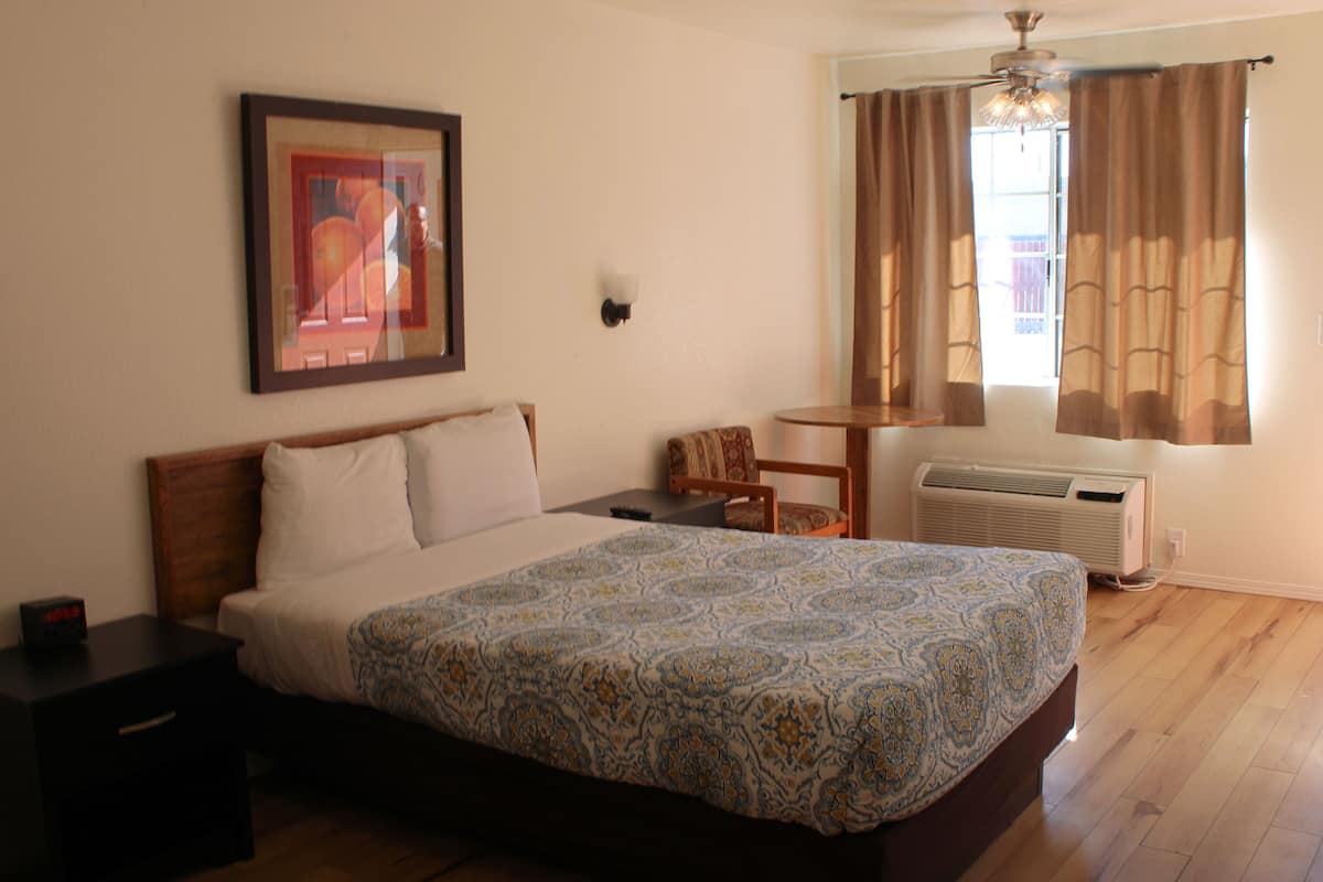 A bedroom with a bed, a chair, a table, a heater, and a window with curtains.