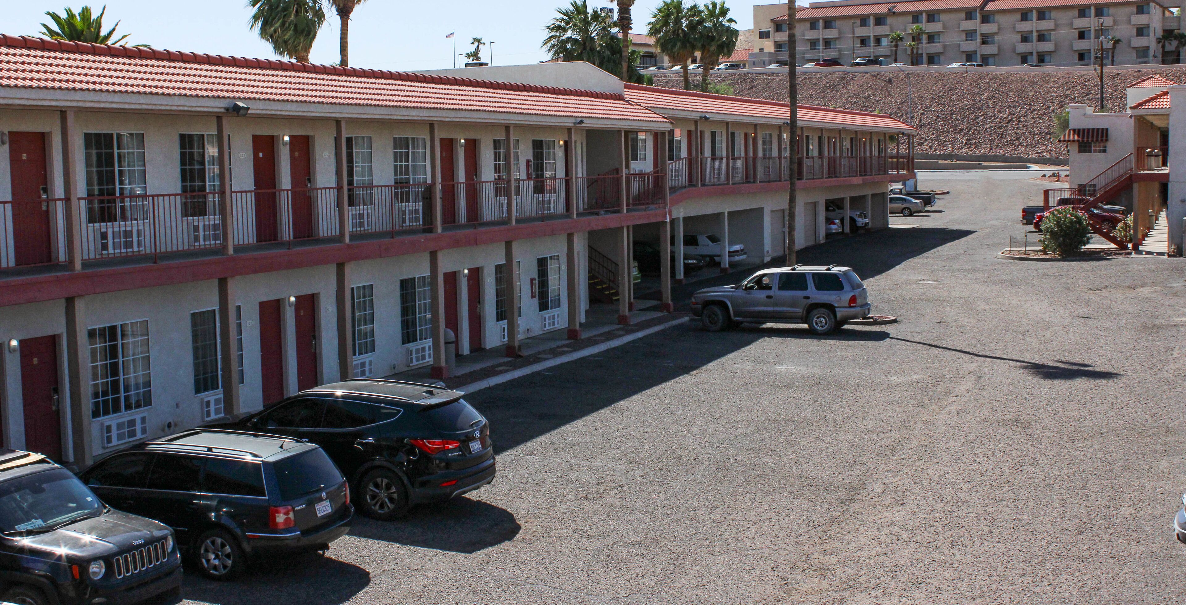 A motel with a red-tiled roof, multiple balconies, and a parking lot with several cars.