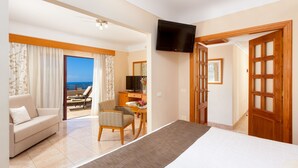 A hotel room with a bed, a sofa, a desk, a TV, and a view of the sea.