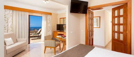 A hotel room with a bed, a sofa, a desk, a TV, and a view of the sea.