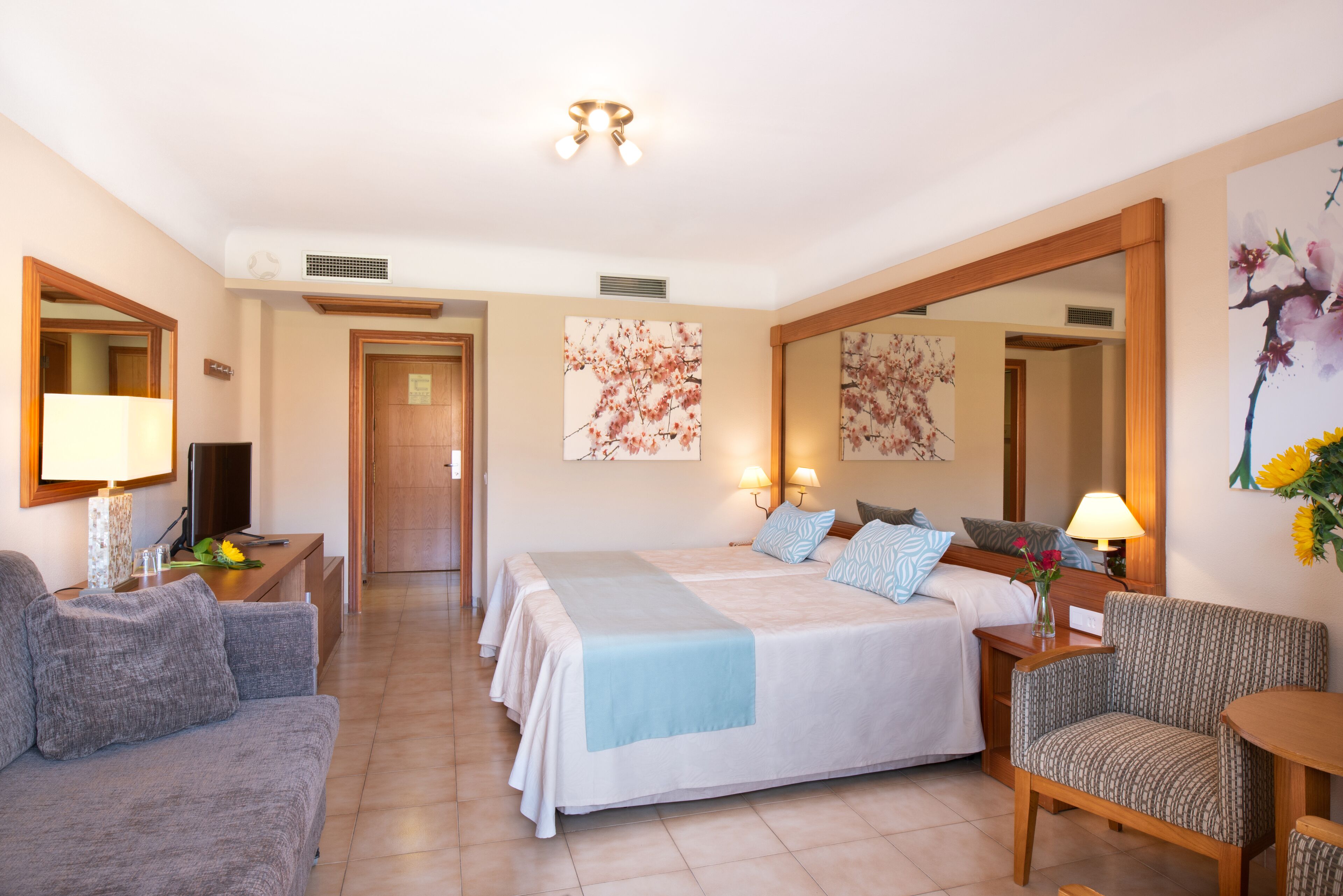 A hotel room with a large bed, two bedside tables with lamps, a sofa, a chair, and a large mirror.
