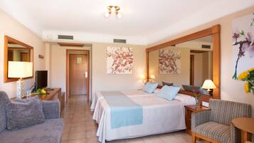 Une chambre d’hôtel avec un grand lit, deux tables de chevet avec des lampes, un canapé, un fauteuil et un grand miroir.
