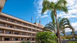 A hotel with multiple balconies, outdoor seating, and palm trees.