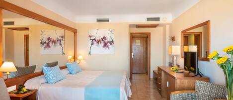 A hotel room with a large bed, a desk, a chair, and artwork on the walls.