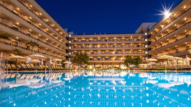 Un hotel con una piscina grande, varios balcones y zonas de estar al aire libre.