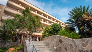 Un hotel con una escalera de piedra, palmeras y un cielo azul despejado.