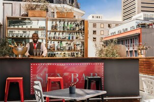 A bar named "SKY BAR" with a variety of liquor bottles, red stools, and a person behind the bar.