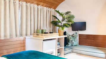 A bedroom with a bed, a bedside table with a lamp, a plant, and a window with curtains.