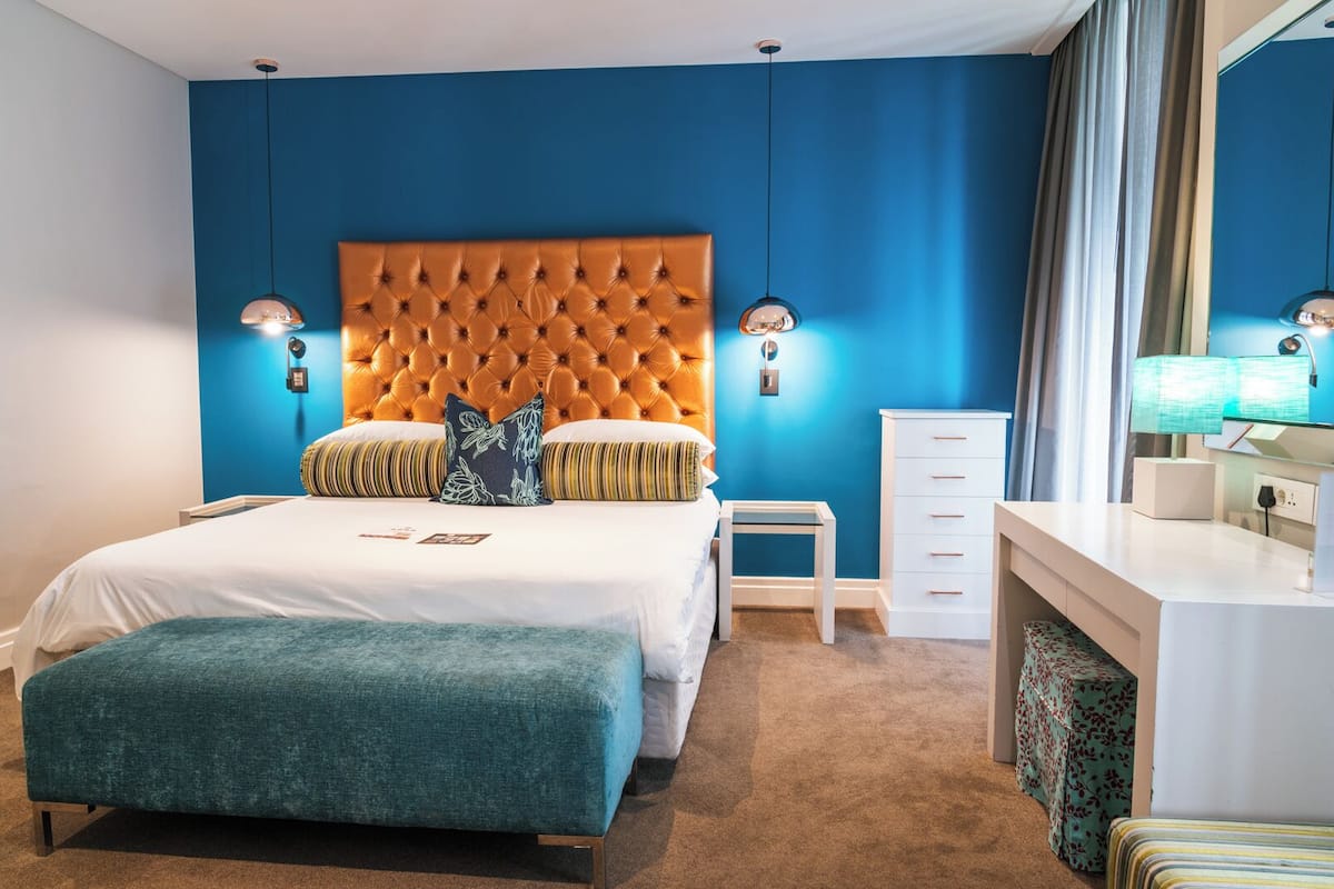 Ein modernes Hotelzimmer mit einer gepolsterten Kopfteil, einem großen Bett, einem Nachttisch, einer Kommode und einem Spiegel.