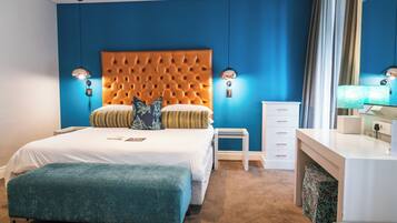 A modern hotel room with a tufted headboard, a large bed, a bedside table, a nightstand, a dresser, and a mirror.