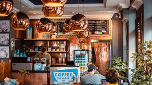Un café avec une enseigne indiquant « Le café, c’est la vodka du matin », un tableau affichant le menu au-dessus, et un coin salon avec un canapé bleu.
