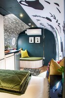 A compact, modern room with a curved ceiling, a bed with a green quilt, a small kitchenette, and a seating area with a green cushion.