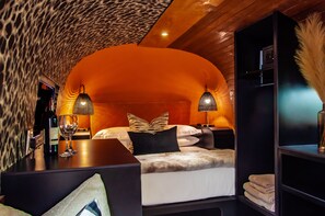 Une chambre confortable avec un plafond cintré, un lit recouvert de draps blancs, deux lampes de chevet et une table de chevet sur laquelle se trouvent une bouteille de vin et un verre.